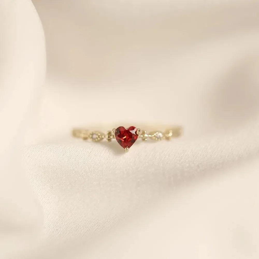 Gold ring with a red heart-shaped gemstone on a beige background