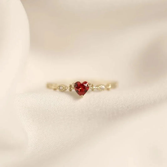 Gold ring with a red heart-shaped gemstone on a beige background